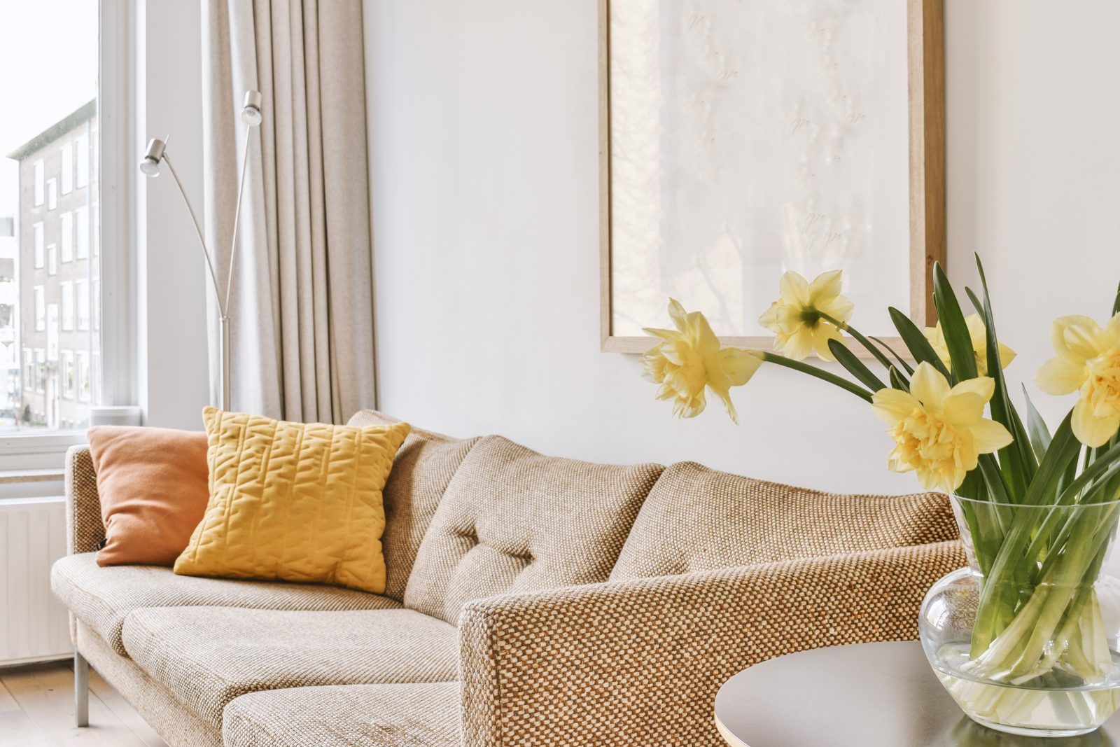 Salón con sofá, cojines, lámpara, cuadro y flores en un jarrón